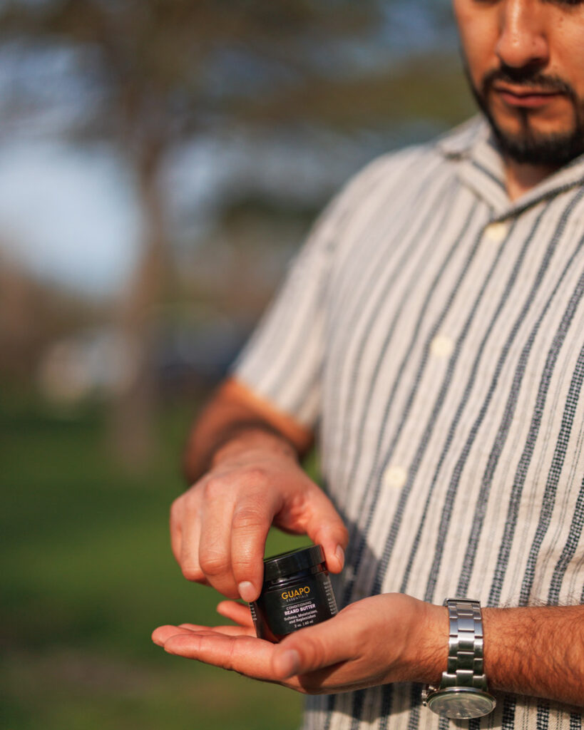 Roy, co-founder of Guapo Essentials, holding a jar of beard butter in a natural outdoor setting.