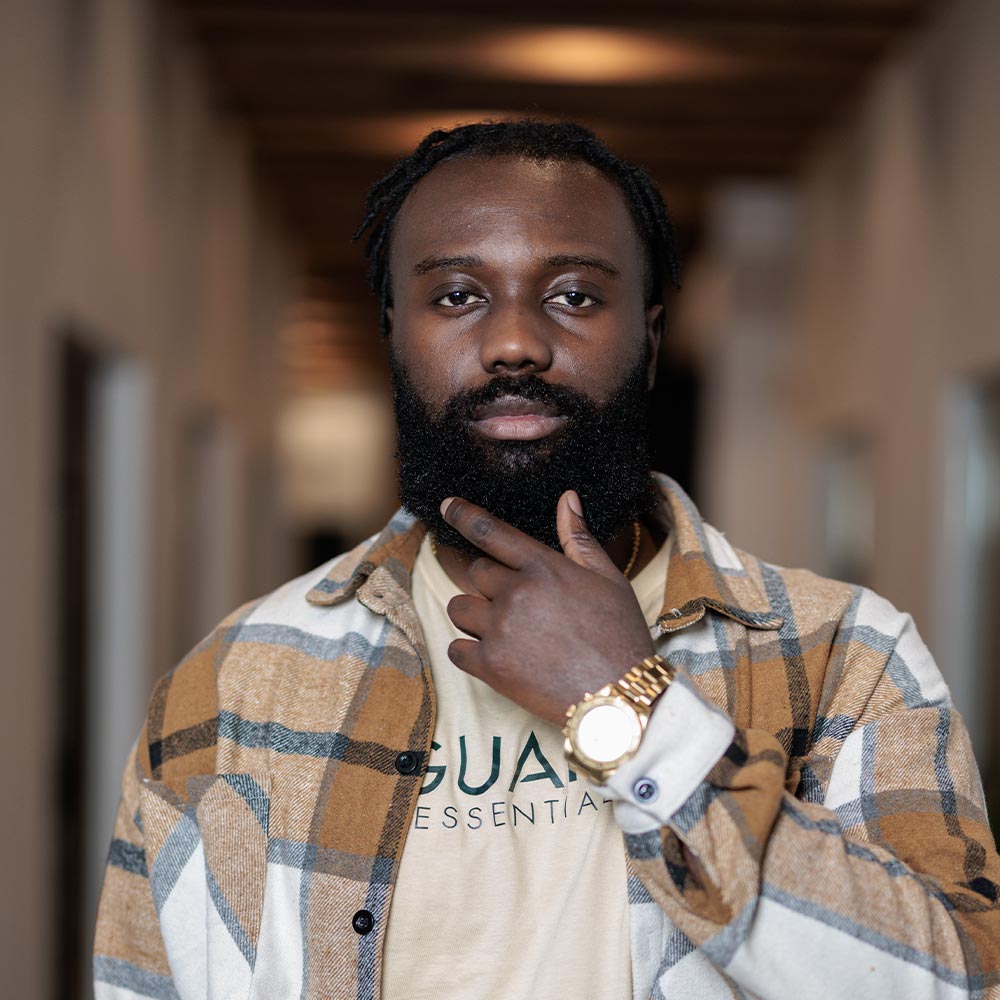 Guapo, co-founder of Guapo Essentials, in casual attire with a confident pose, resting his hand on his chin and pointing to the side.